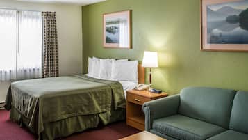 A hotel room with a bed, a nightstand with a lamp, a sofa, and two framed pictures on the wall.