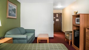Una habitación pequeña y amoblada con un sofá verde, una mesa de madera, un sillón pequeño, una cama y un armario de madera con un televisor.