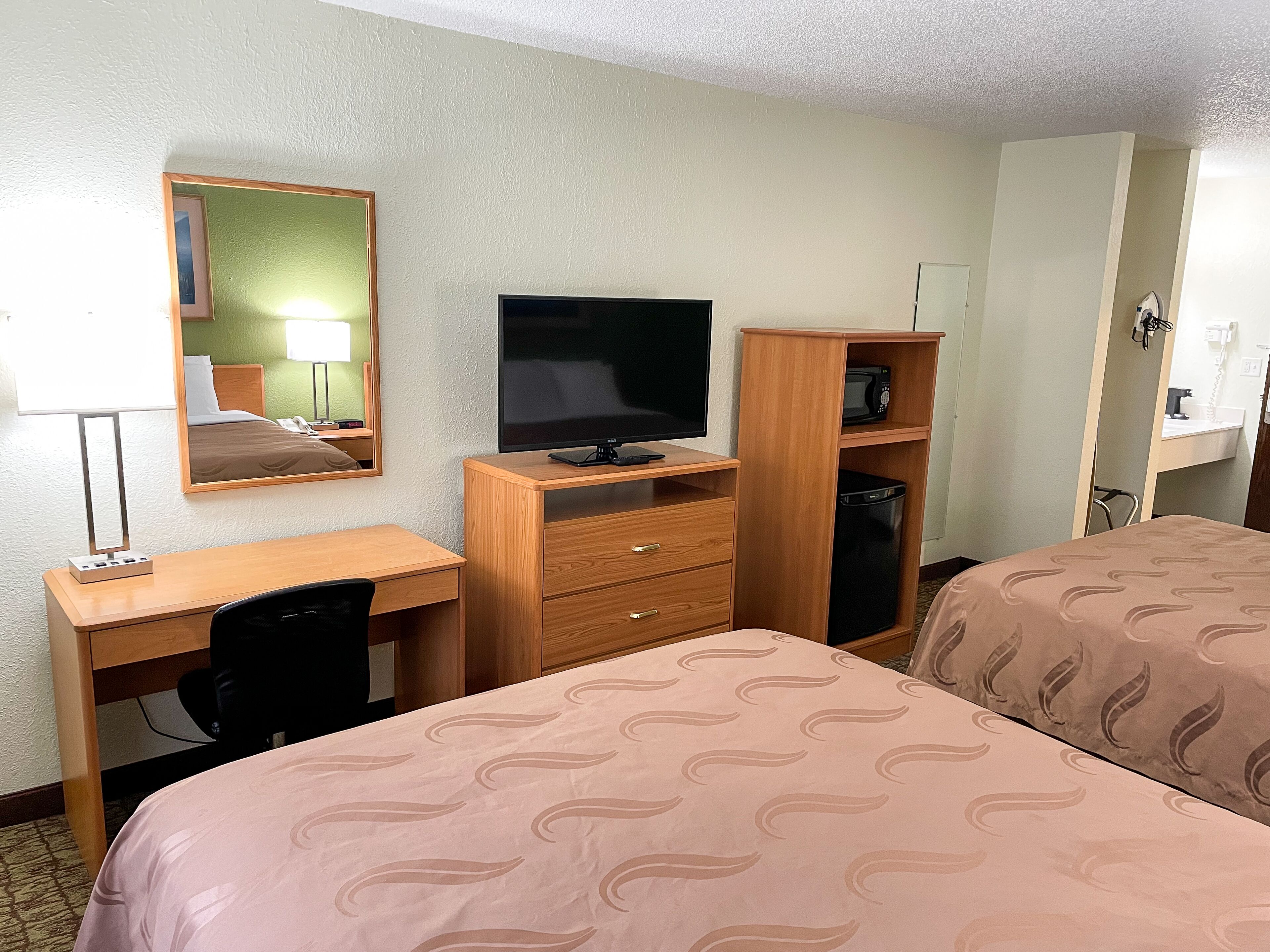 A hotel room with a bed, a desk with a computer, a TV, a mirror, and a wardrobe.