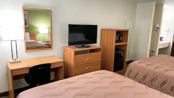 A hotel room with a bed, a desk with a computer, a TV, a mirror, and a wardrobe.