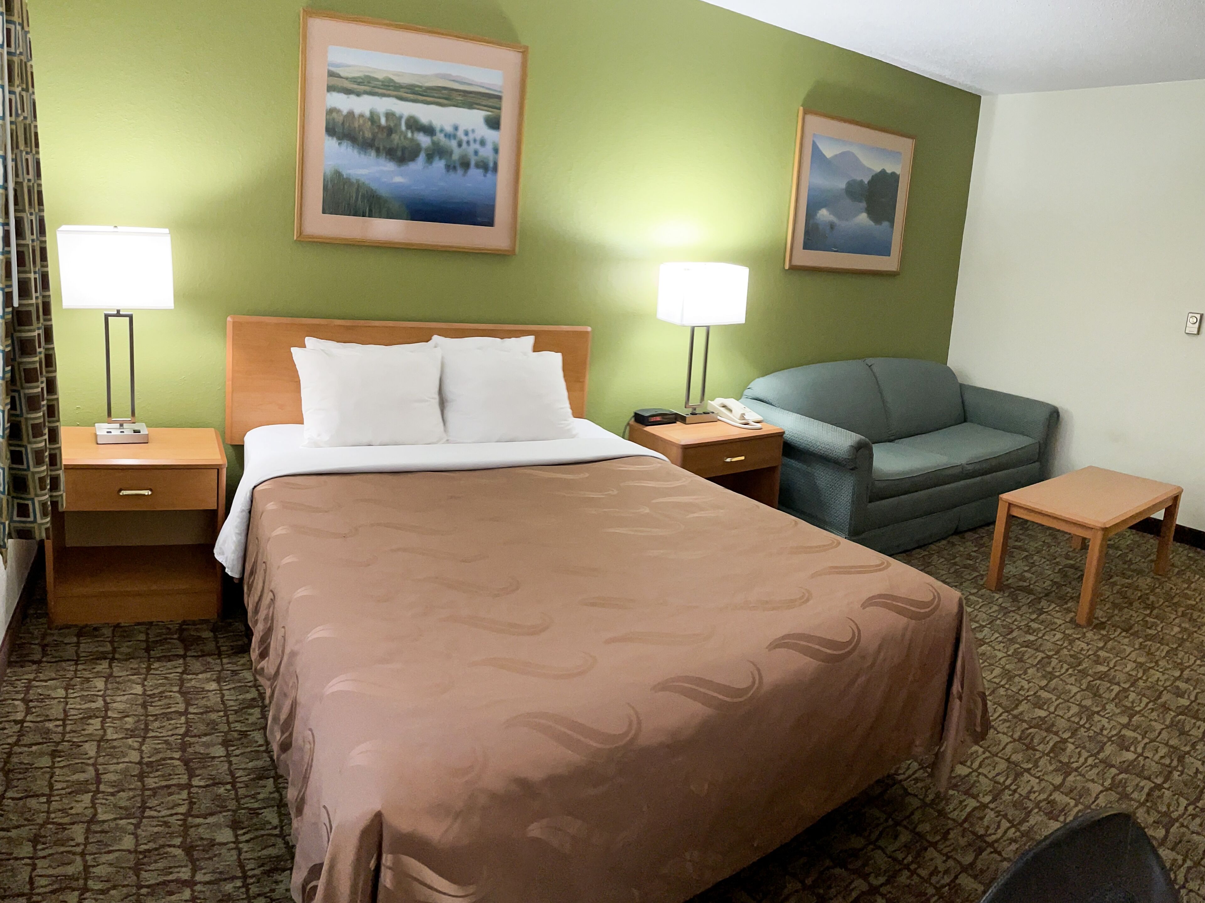 A hotel room with a bed, two nightstands, a desk, a chair, and two wall-mounted lamps.