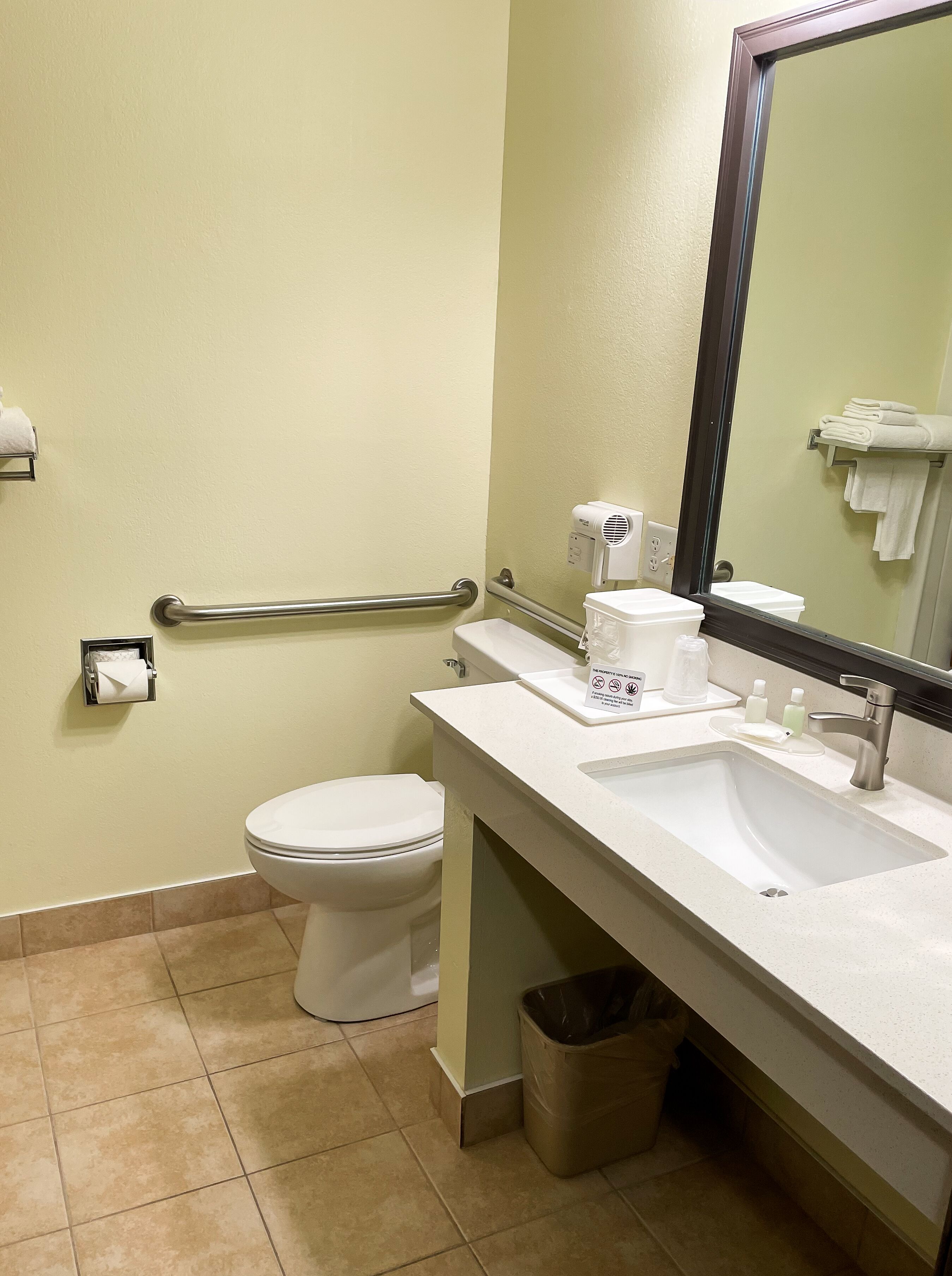 A bathroom with a toilet, sink, mirror, towel rack, and hand dryer.