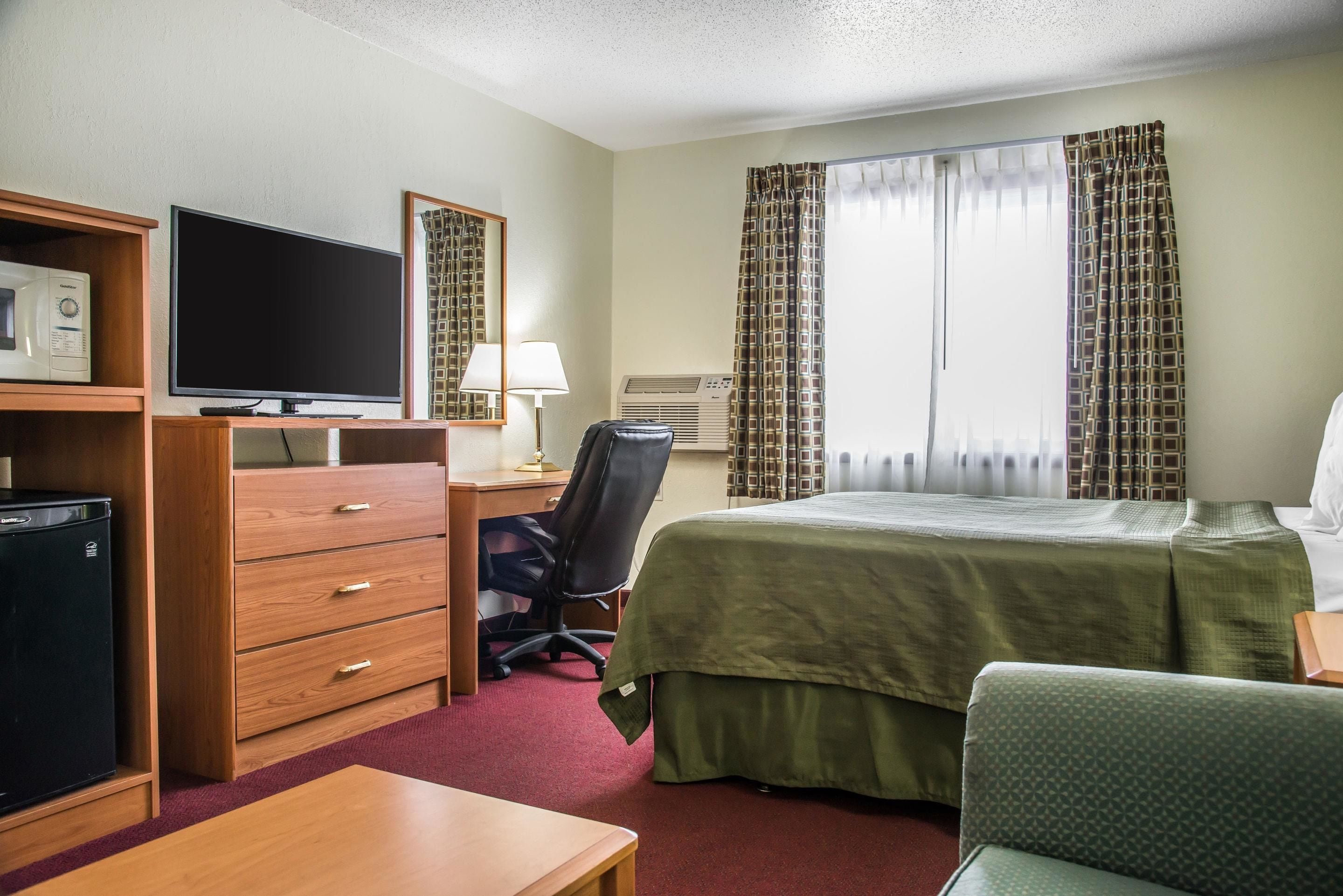 A hotel room with a bed, a desk with a computer, a television, a microwave, and a chair.