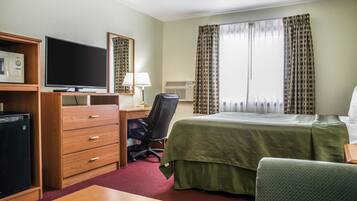 A hotel room with a bed, a desk with a computer, a television, a microwave, and a chair.
