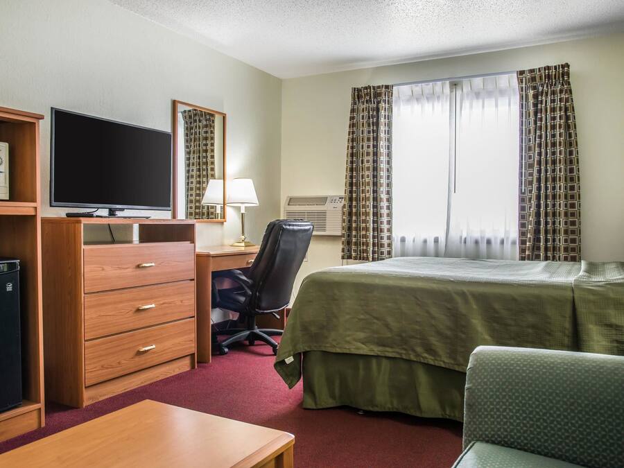 A hotel room with a bed, a desk with a computer, a television, a microwave, and a chair.