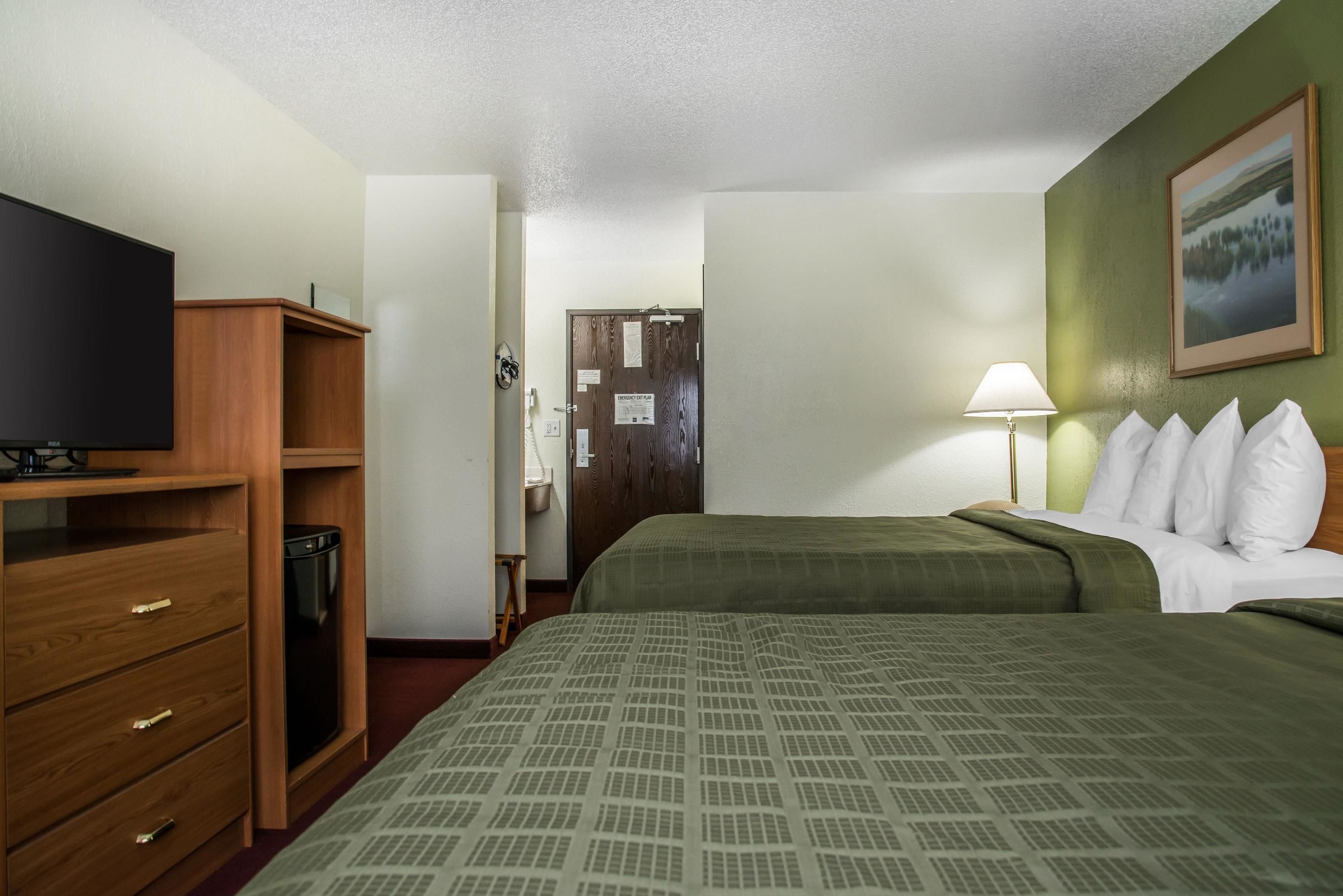 Una camera d'albergo con un letto, una televisione, una cassettiera in legno, una lampada e un quadro appeso al muro.