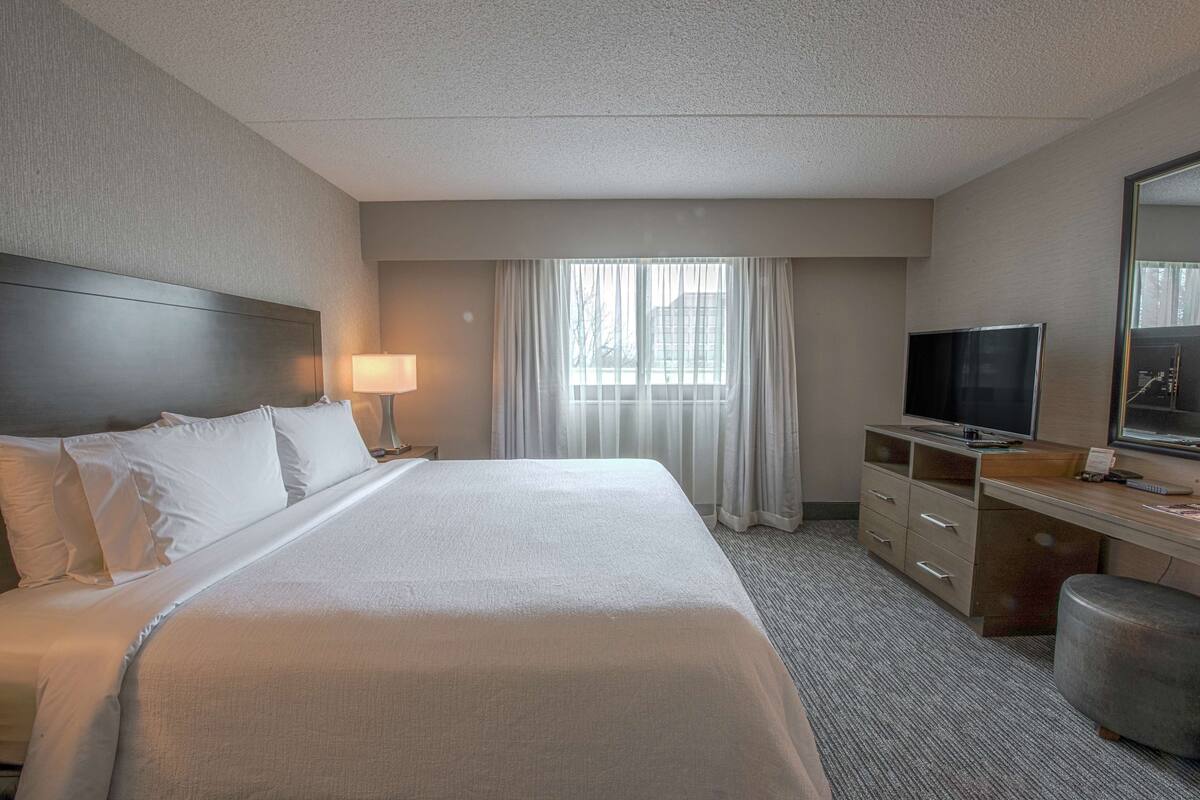 Habitación de hotel con una cama grande, un escritorio con televisor y una ventana con cortinas.