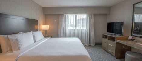 A hotel room with a large bed, a desk with a television, and a window with curtains.