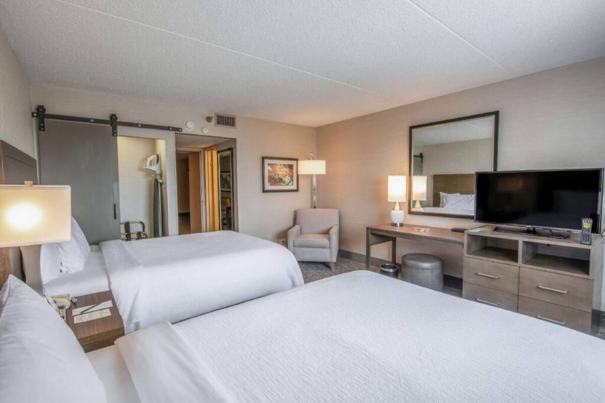 Una habitación de hotel con dos camas, un escritorio, una silla, un televisor y un espejo.