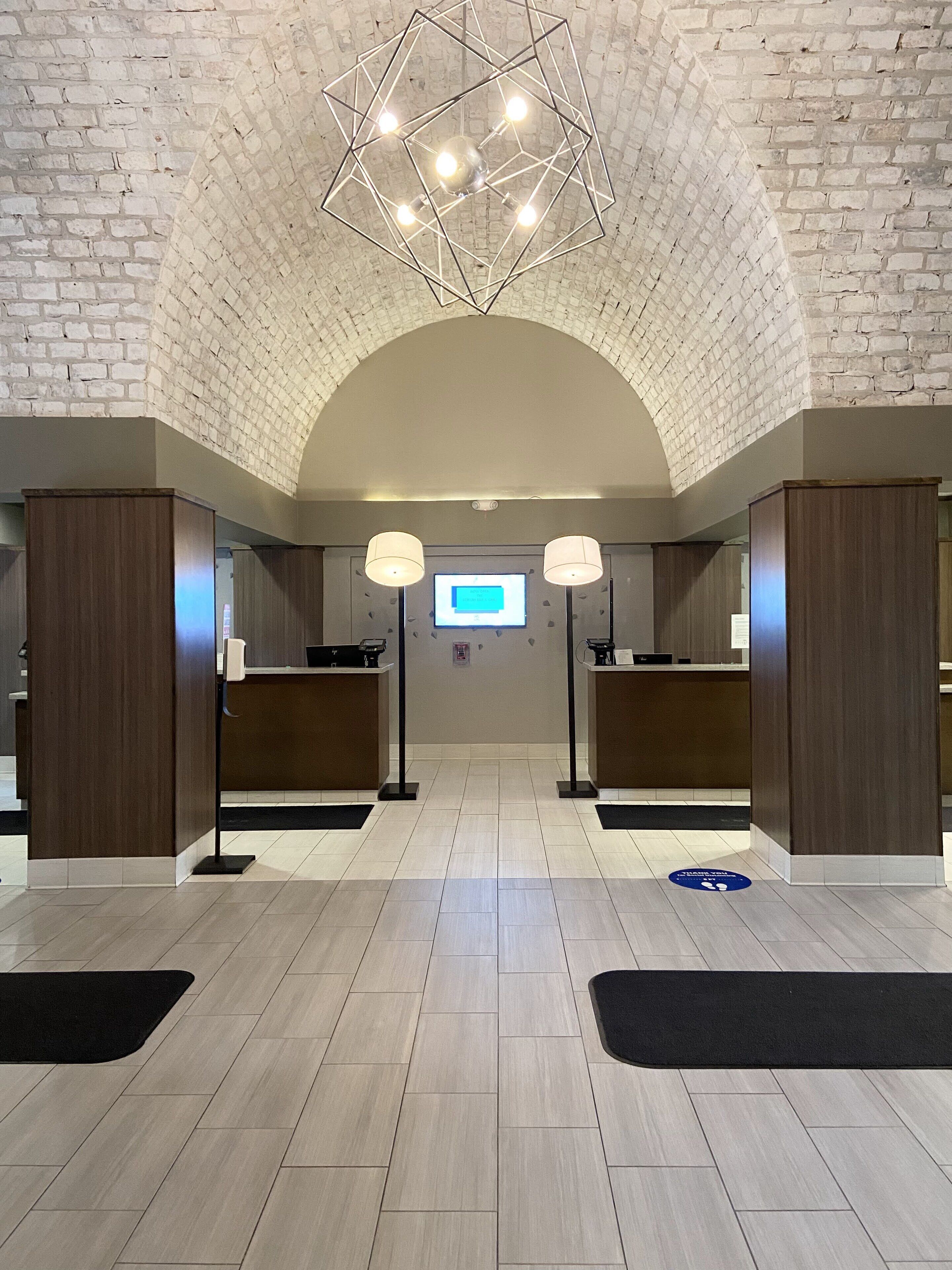 A reception area with a brick wall, a geometric light fixture, and a digital display.