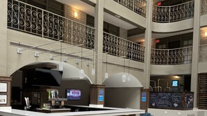 A multi-level hotel lobby with a central bar area, seating arrangements, and a digital screen displaying information. - Embassy Suites by Hilton Chicago Schaumburg Woodfield (Schaumburg)