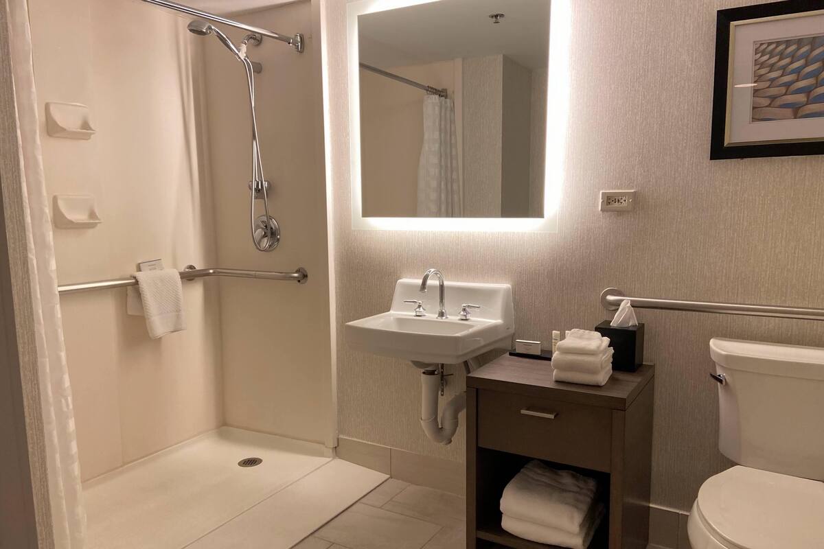 Un baño moderno con cabina de ducha, lavamanos, inodoro y tocador pequeño con toallero.