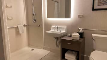 Un baño moderno con cabina de ducha, lavamanos, inodoro y tocador pequeño con toallero.