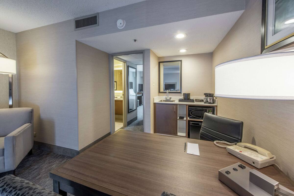 Habitación de hotel con una mesa de conferencias de madera, un teléfono, una lámpara de escritorio y un área de descanso con un sofá y sillones.