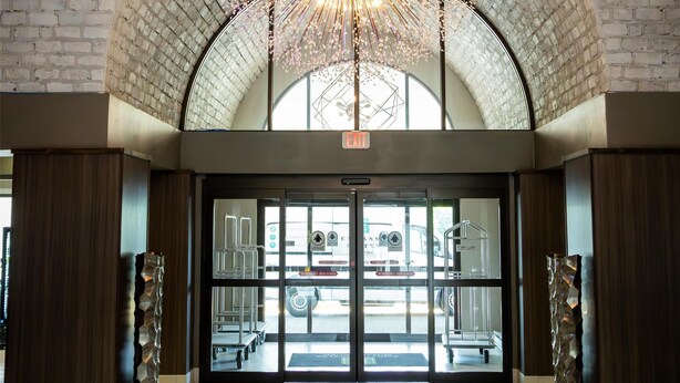 A spacious lobby with a high arched brick ceiling, a central chandelier, and a view of the parking area through glass doors. - Embassy Suites by Hilton Chicago Schaumburg Woodfield (Schaumburg)