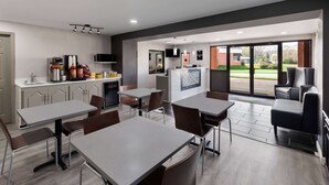 A modern dining area with tables and chairs, a kitchen area with appliances, and a large window providing a view of the outdoors. - Days Inn by Wyndham Childersburg/Sylacauga (Childersburg)