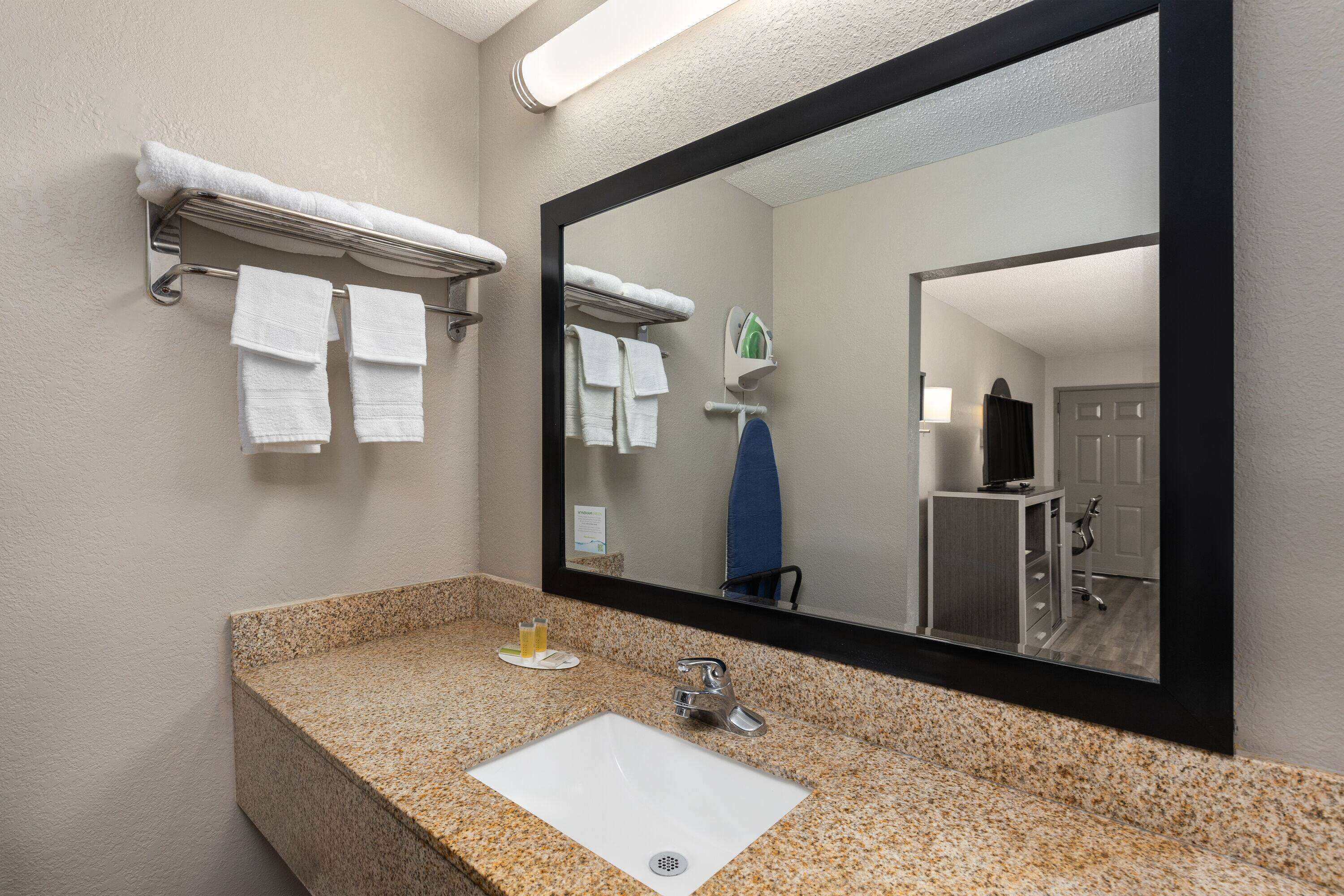 Une salle de bain avec un lavabo doté d’un plan de travail en granit, un miroir et un porte-serviettes avec plusieurs serviettes.