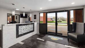 A reception area with a white tiled counter, a black-framed glass partition, and a black chair. - Days Inn by Wyndham Childersburg/Sylacauga (Childersburg)