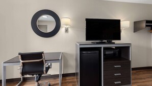 A hotel room with a desk, chair, television, and a minibar. - Days Inn by Wyndham Childersburg/Sylacauga (Childersburg)