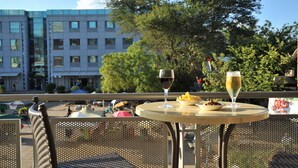 A table with two glasses of wine and a plate of food on an outdoor terrace with a city view. - Cresta President (Gaborone)