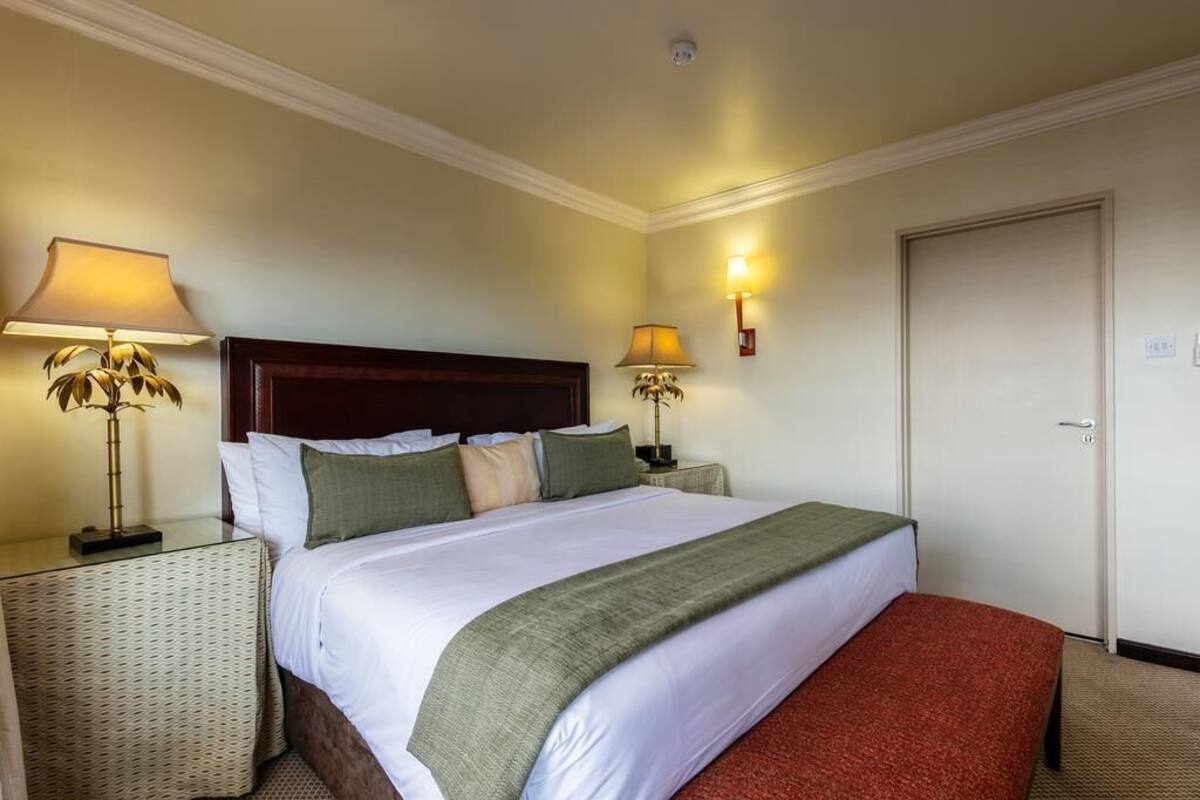 A hotel room with a large bed, two bedside tables with lamps, a door, and a wall-mounted light fixture.