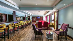 A spacious lobby with a long bar area, multiple seating options including chairs and sofas, and a television mounted on the wall. - Cresta President (Gaborone)