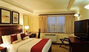 Ein Hotelzimmer mit Bett, Fernseher, Schreibtisch, Lampe und einem Fenster mit Vorhängen.