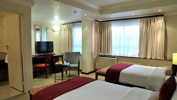 A hotel room with two beds, a desk with a television, a chair, and a window with curtains.