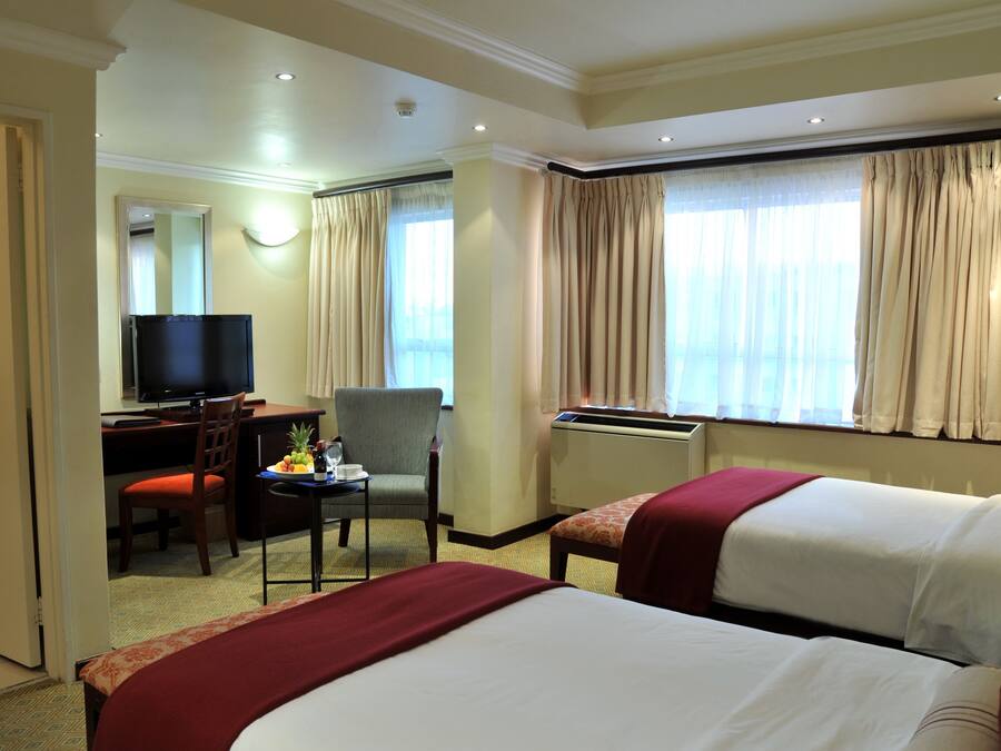 A hotel room with two beds, a desk with a television, a chair, and a window with curtains.