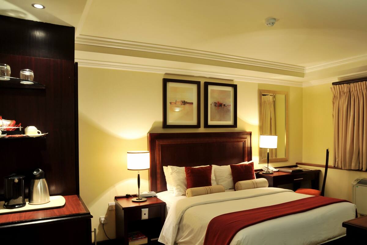 A hotel room with a large bed, two bedside tables, a desk, a window with curtains, and two framed pictures on the wall.