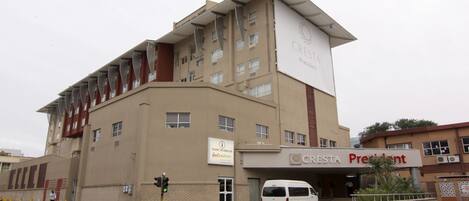 Hotel A CRESTA President, com design moderno, exibindo uma placa de identificação e uma carrinha branca estacionada em frente.