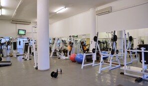 Ein Fitnessstudio mit verschiedenen Trainingsgeräten, darunter Kraftgeräte, Kurzhanteln und Trainingsbälle.