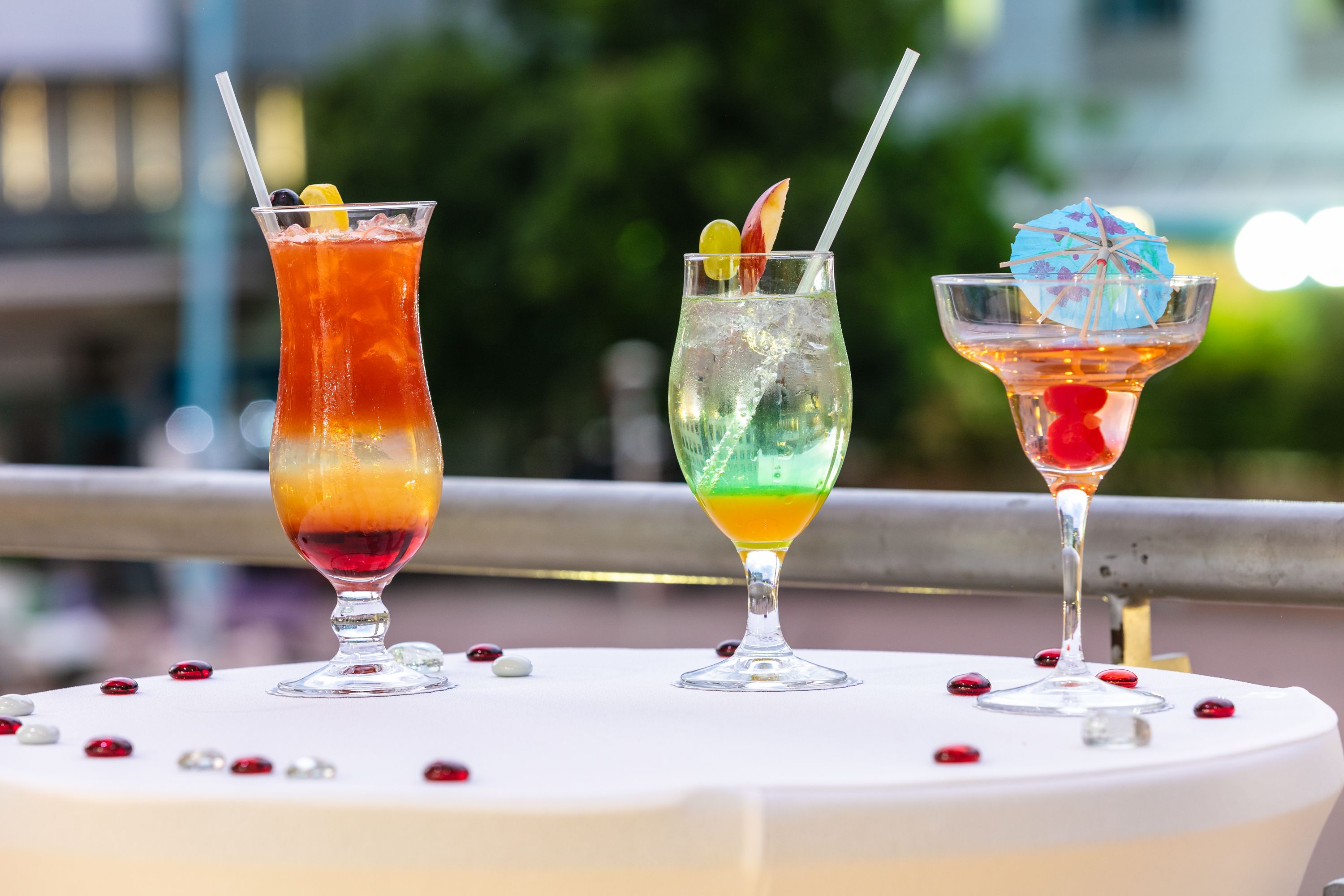 Three cocktails on a table with a railing in the background.