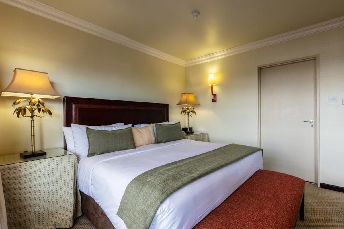 A hotel room with a large bed, two bedside tables with lamps, a door, and a wall-mounted light fixture.
