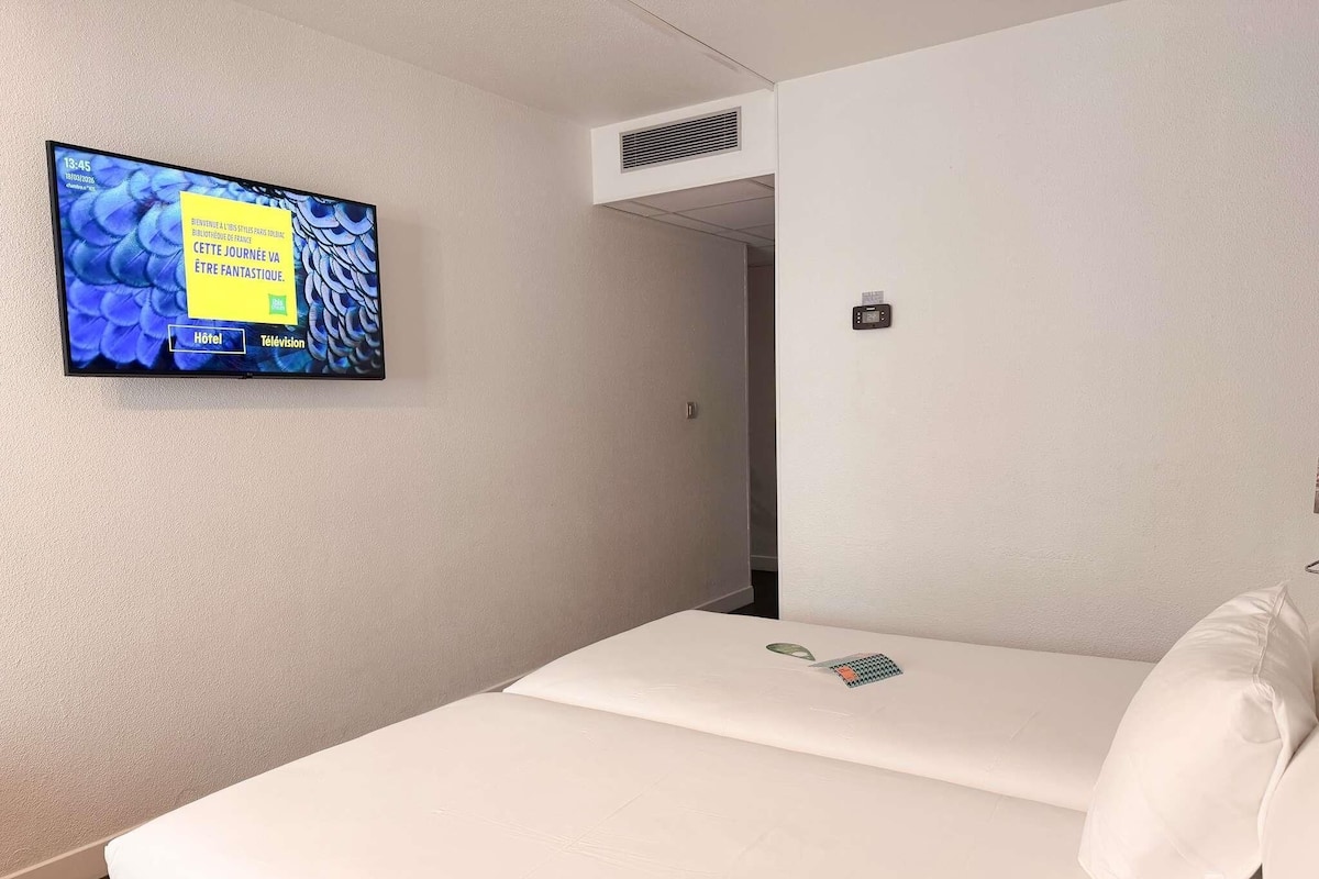 Habitación de hotel con una cama, un televisor montado en la pared y un termostato en la pared.