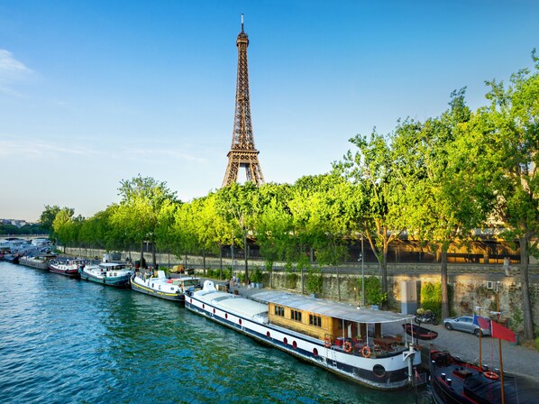 A river with boats, a large tower in the background, and trees along the riverbank. - ibis Styles Paris Tolbiac Bibliotheque (Paris)