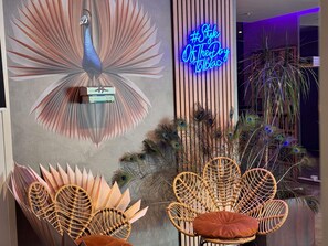 Et værelse med vægkunst i påfuglefjeder-design, et neonlys og fletstole.