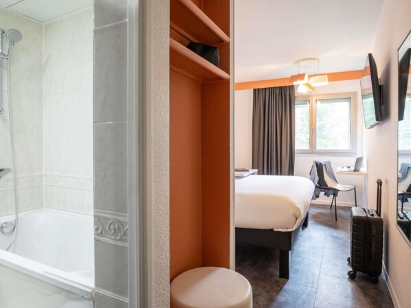 A hotel room with a shower, a bed, a desk with a laptop, a chair, and a suitcase. - ibis Styles Paris Tolbiac Bibliotheque (Paris)