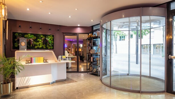 A modern reception area with a curved glass entrance, a reception desk, and a green wall decoration. - ibis Styles Paris Tolbiac Bibliotheque (Paris)