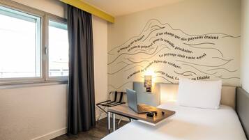 Habitación de hotel con cama, escritorio con una computadora portátil, una silla, ventana con cortinas y un diseño decorativo en la pared.