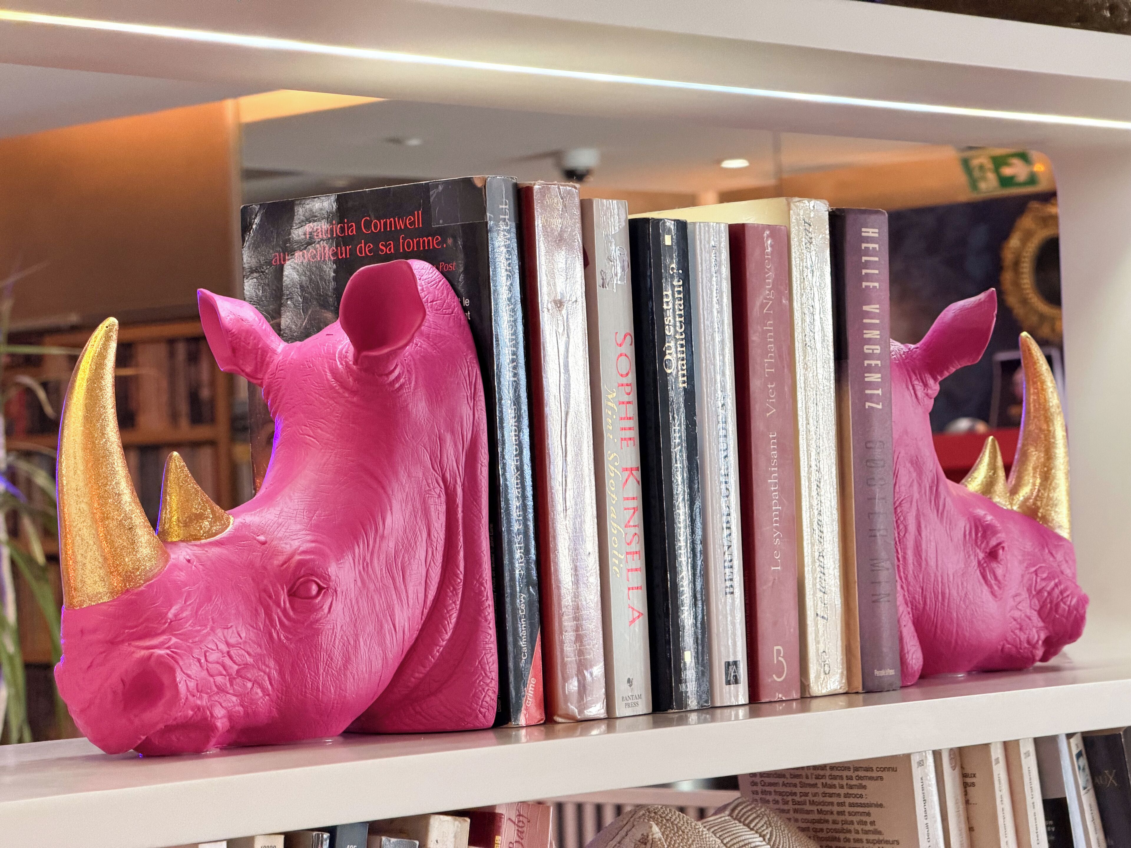 Une bibliothèque remplie de livres et ornée de deux sculptures de rhinocéros roses.