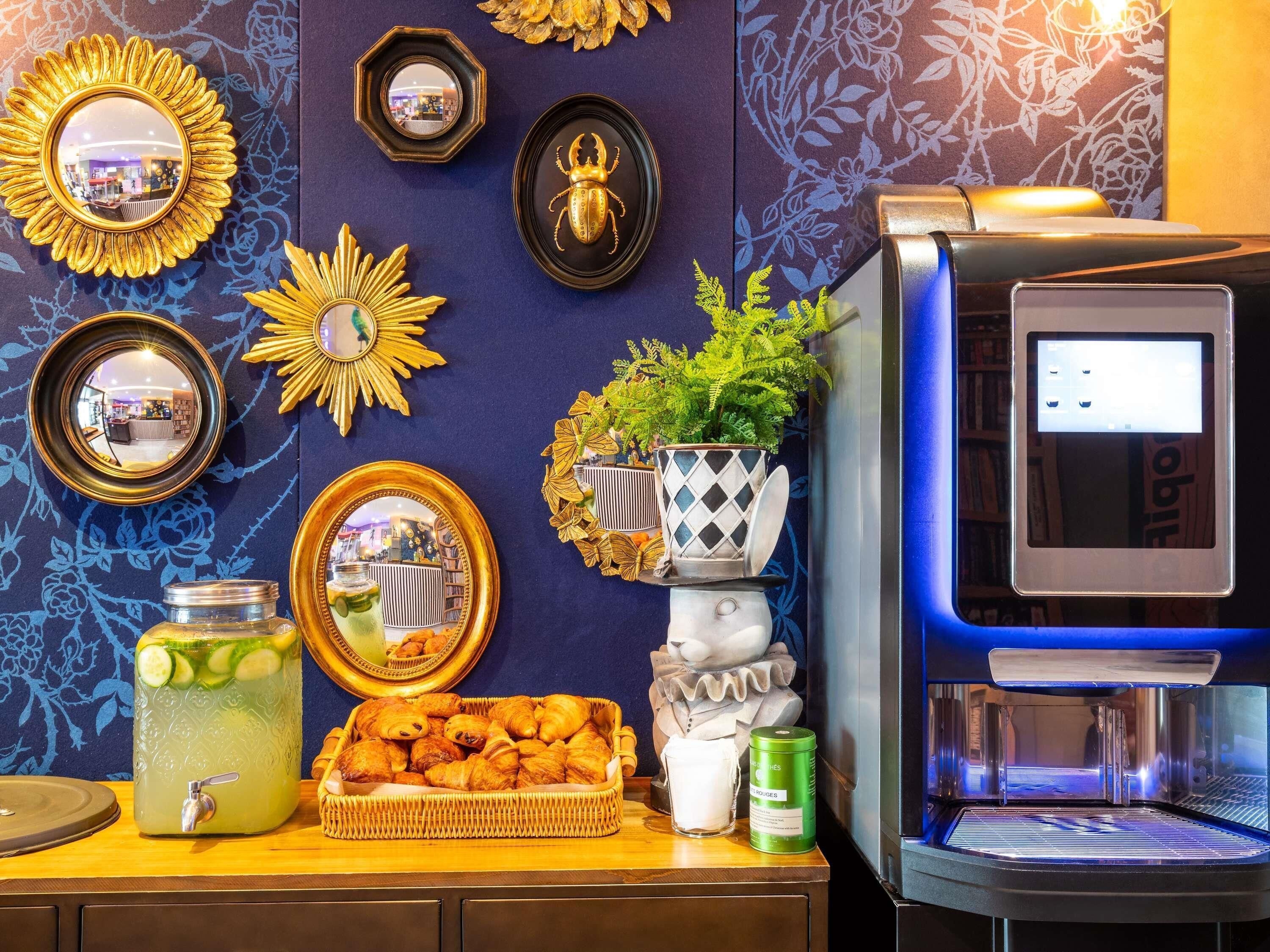 Una barra con dispensador de bebidas, máquina de café, espejos decorativos y una exhibición de pasteles.