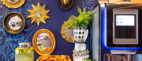 Una barra con dispensador de bebidas, máquina de café, espejos decorativos y una exhibición de pasteles.