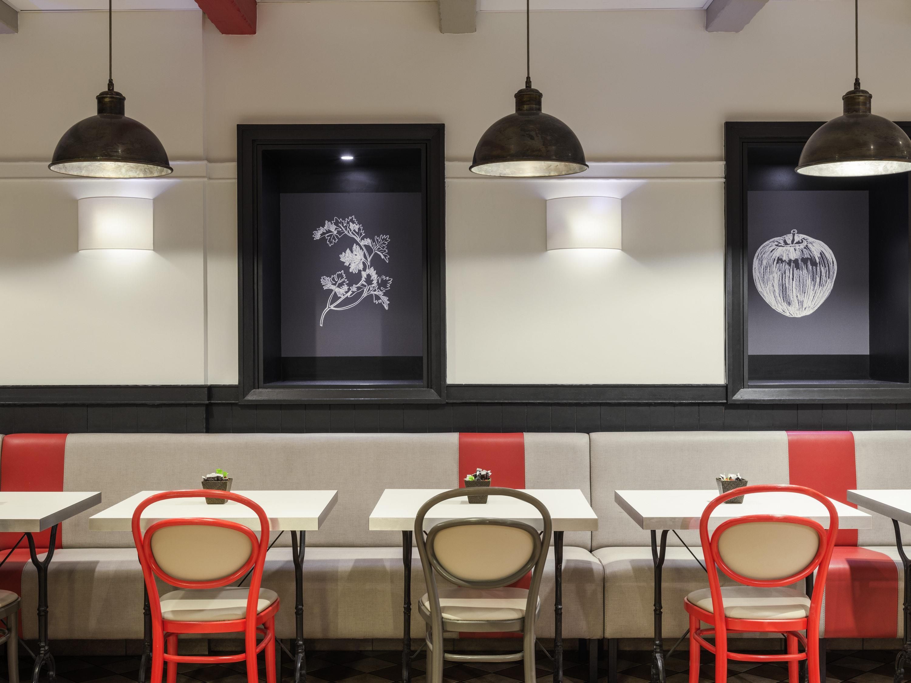 A restaurant interior with booths, red and grey chairs, pendant lighting, and framed artwork on the wall.