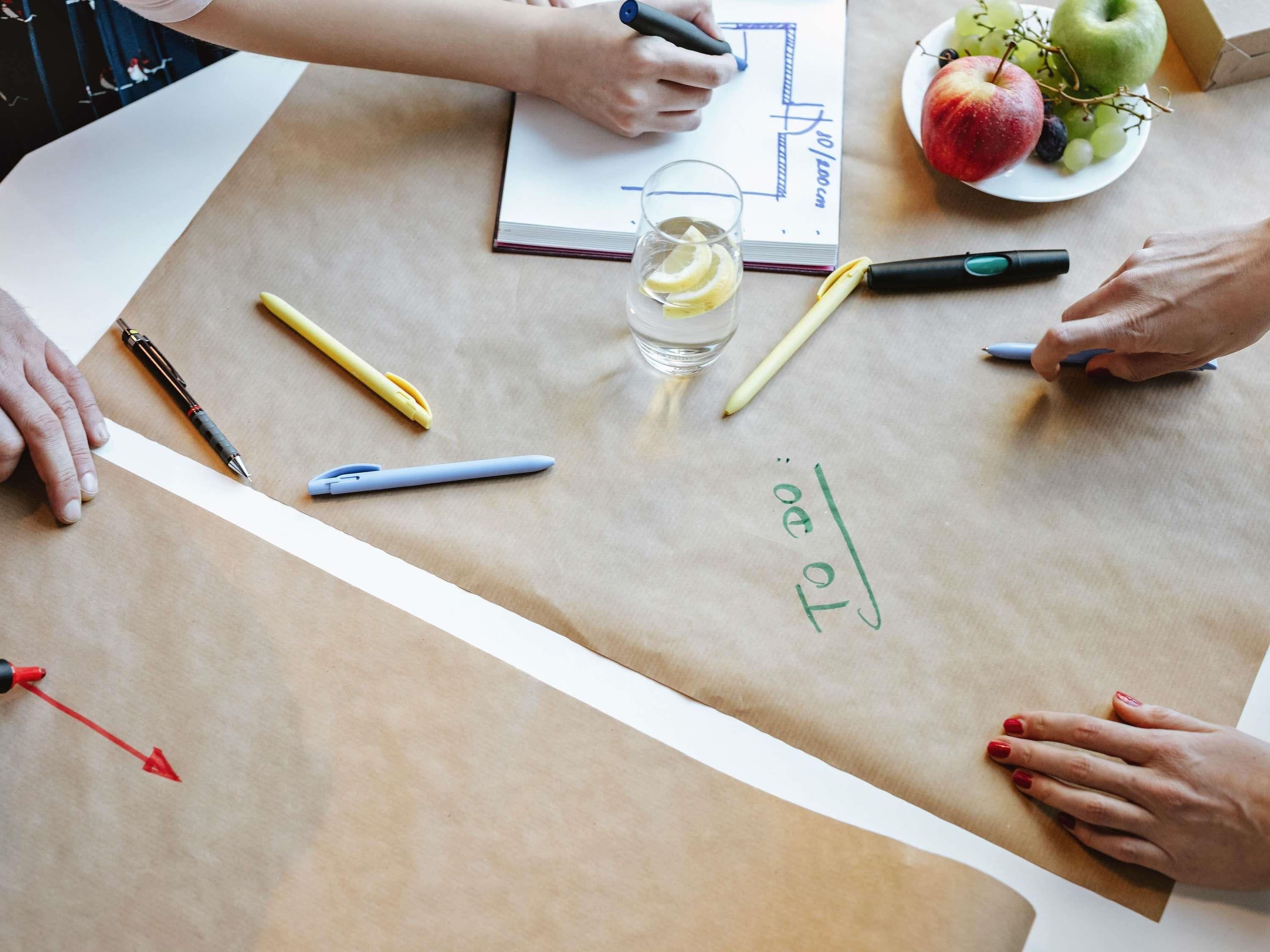 Une table avec un carnet, des stylos, un verre d’eau et une assiette de fruits.