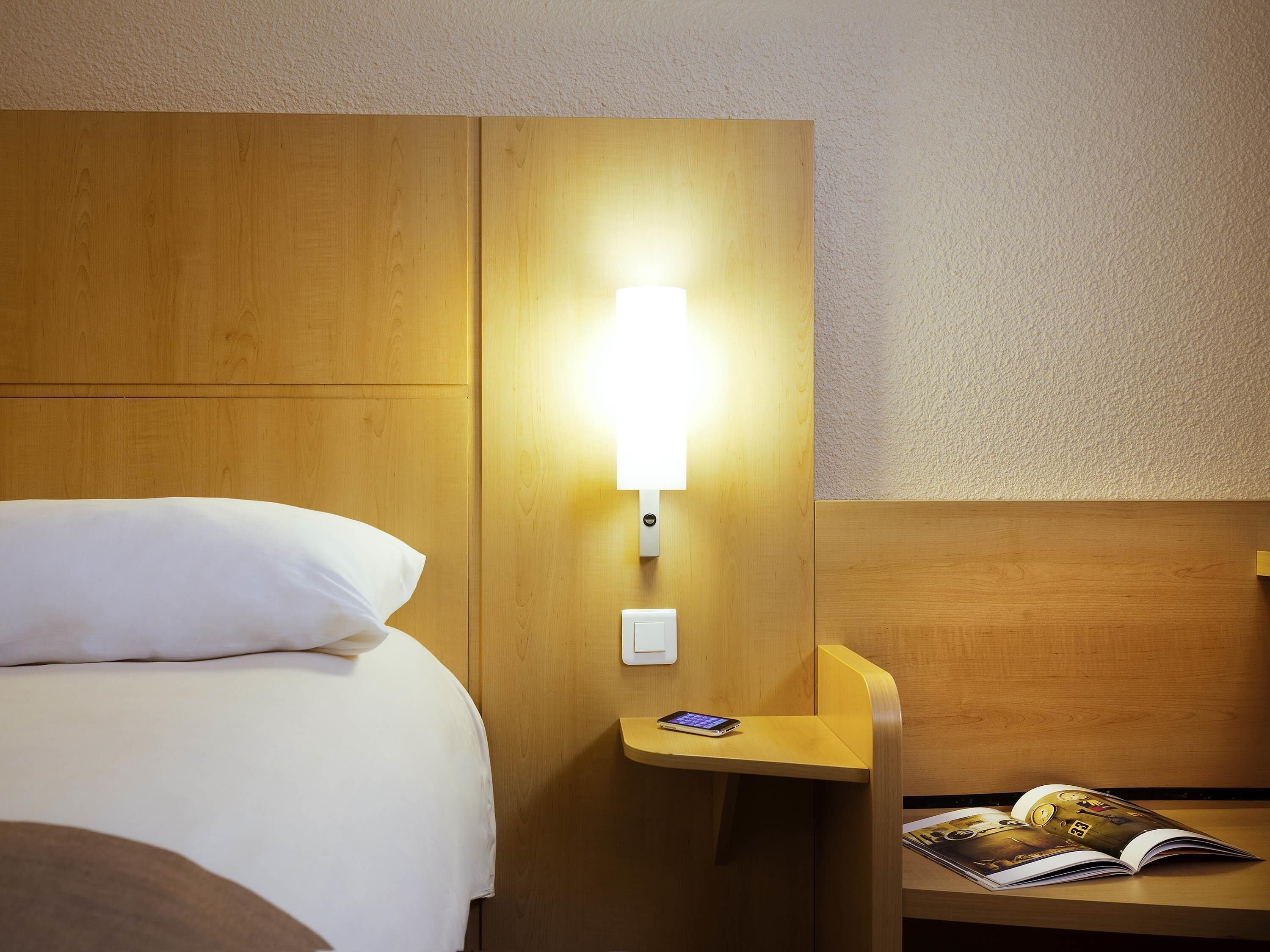 Une chambre d’hôtel avec un lit, une table de chevet avec une lampe et un magazine posé sur la table.