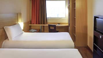 A hotel room with two beds, a desk, a chair, a TV, and a window with curtains.