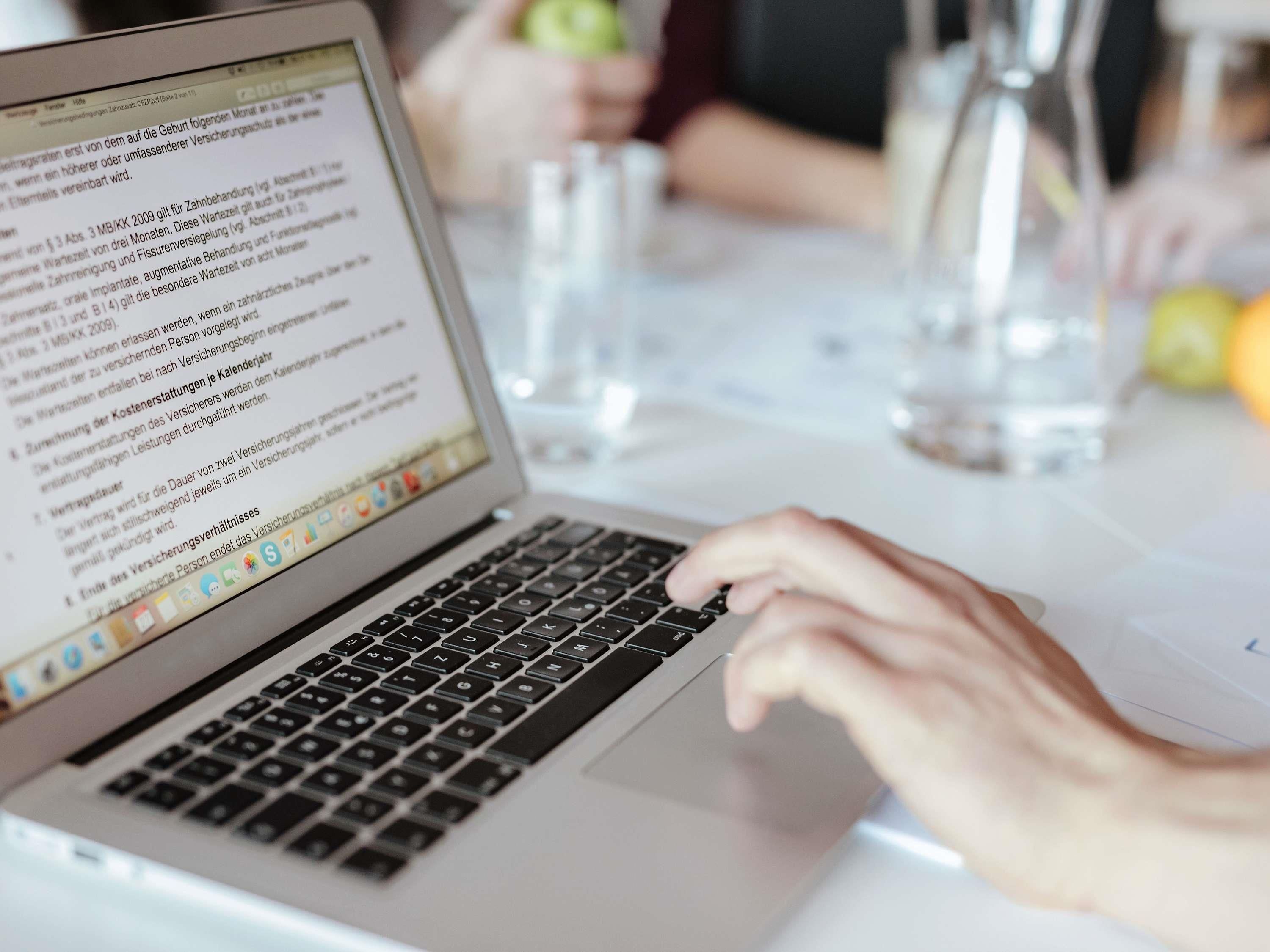 A laptop on a table with a person typing.