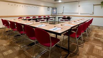 Une salle de conférence équipée de plusieurs tables, de chaises rouges et d’un tableau blanc.