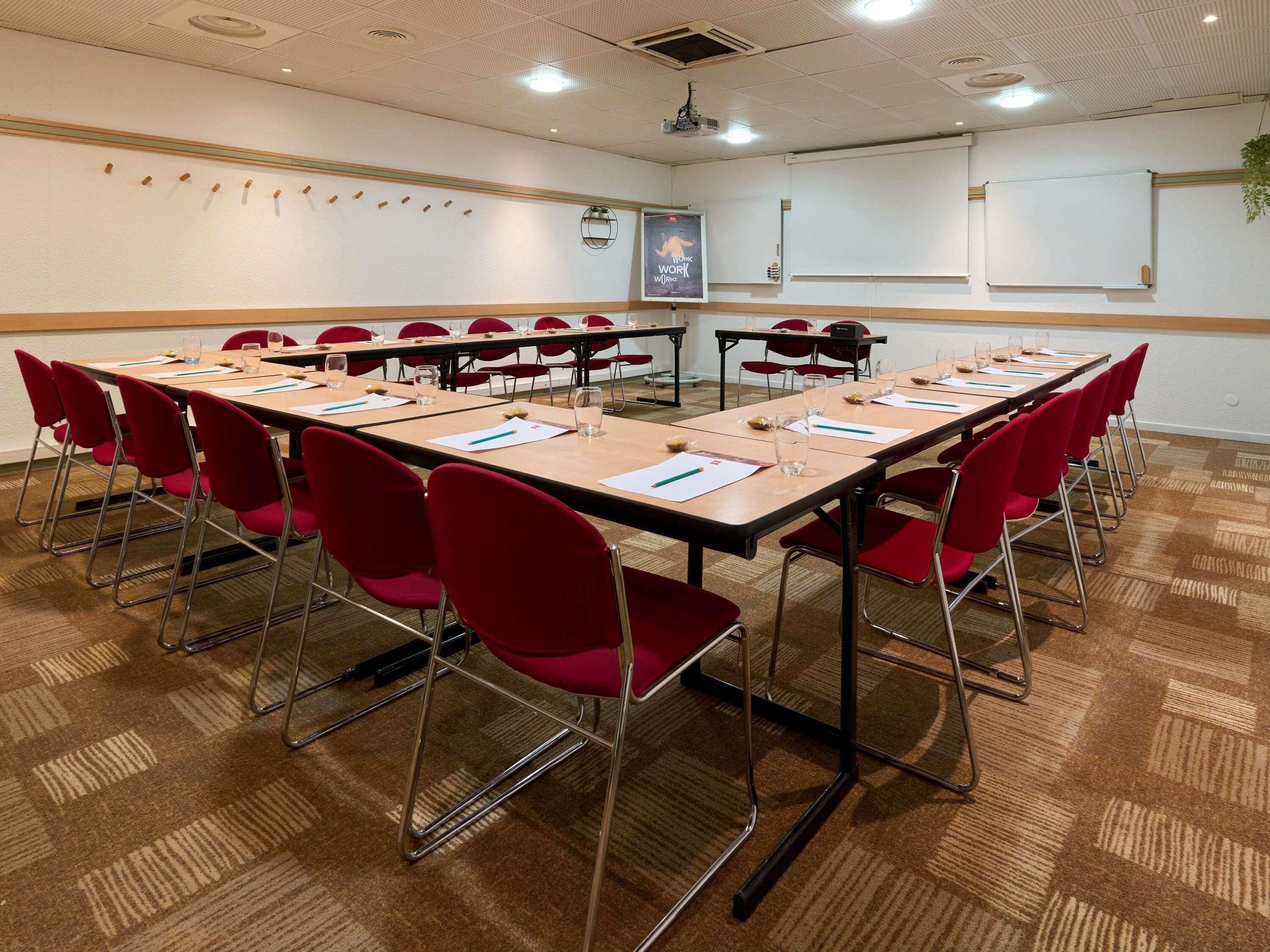 Un salón de conferencias con varias mesas, sillas rojas y una pizarra.